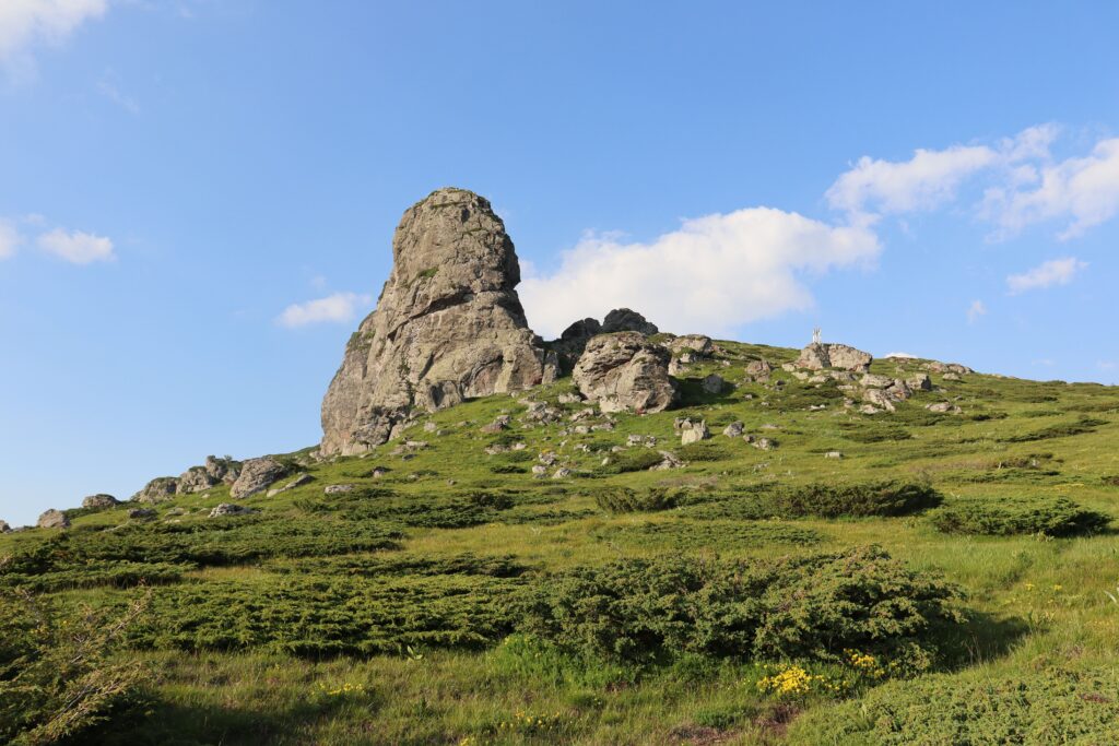 A stunning rocky hill under clear skies, surrounded by lush greenery.